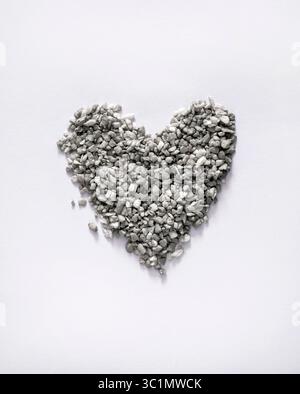 Cuore di pietra. Simbolo dell'amore realizzato in pietre di ghiaia frantumate. Sfondo bianco. Nessun testo. Piccoli ciottoli grigi disposti a forma di cuore. Foto Stock