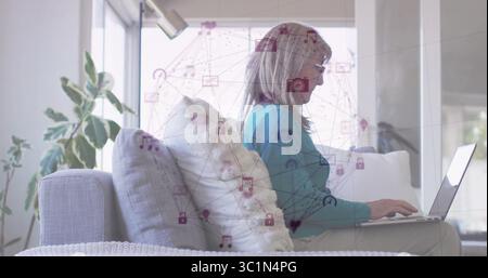 Donna che scrive indossa un maglione di tè appoggiato sul divano nel soggiorno, con icone di rete e laptop Foto Stock