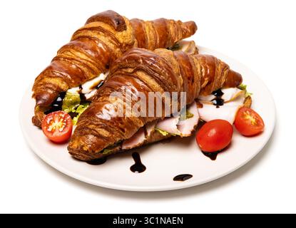 Due deliziosi croissant biologici freschi appena sfornati con prosciutto, formaggio, salsa al pesto e pomodori su un piatto bianco di ceramica isolato su bianco Foto Stock