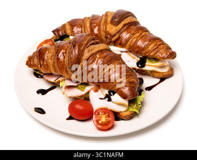 Due deliziosi croissant biologici freschi appena sfornati con prosciutto, formaggio, salsa al pesto e pomodori su un piatto bianco di ceramica isolato su bianco Foto Stock