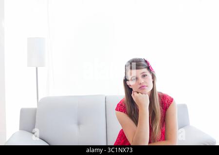 Donna seduta sul divano che indossa un abito rosso con lampada da terra con ombra bianca, tende, spazio per fotocopie Foto Stock