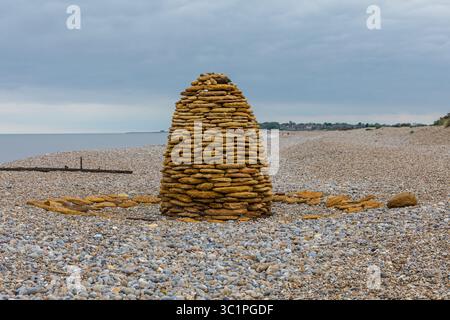 Un cairn a forma di alveare fatto di pietre impilate su una spiaggia di ciottoli, che fonde materiali naturali ed espressioni artistiche sulla costa britannica. Foto Stock
