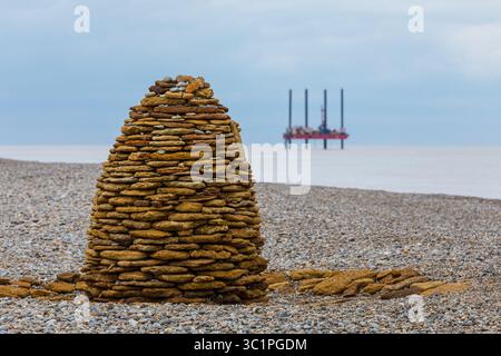 Un cairn a forma di alveare fatto di pietre impilate su una spiaggia di ciottoli, che fonde materiali naturali ed espressioni artistiche sulla costa britannica. Foto Stock
