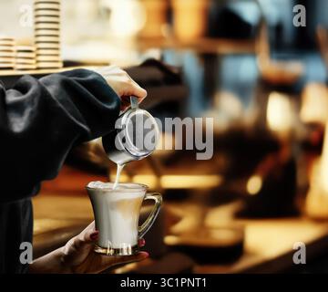 Il barista versa un ricco latte montato in una tazza di bicchiere, realizzando un'arte del cappuccino in un accogliente bar Foto Stock