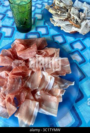 Tagli di salato tipico prosciutto crudo italiano e salame chiamato finocchiona in un piatto blu. Salame tradizionale della cucina italiana. Direttamente sopra. Foto Stock