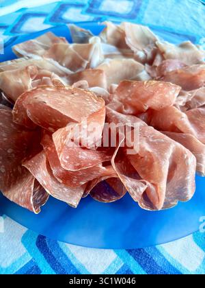 Tagli di salato tipico prosciutto crudo italiano e salame chiamato finocchiona in un piatto blu. Salame tradizionale della cucina italiana. Direttamente sopra. Foto Stock