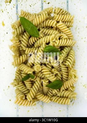 Fusilli freddi italiani con salsa al pesto e foglie di basilico fresco in un recipiente di vetro. Piatto estivo. Direttamente sopra. Foto Stock