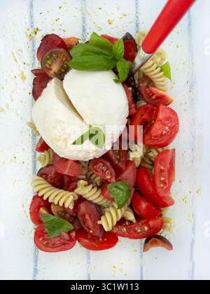 Fusilli freddi italiani con salsa al pesto, pomodori, mozzarella e foglie di basilico fresco in un recipiente di vetro. Piatto estivo. Direttamente sopra. Foto Stock
