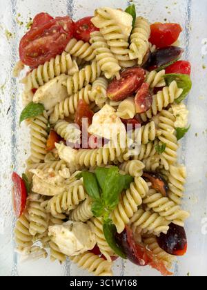 Fusilli freddi italiani con salsa al pesto, pomodori, mozzarella e foglie di basilico fresco in un recipiente di vetro. Piatto estivo. Direttamente sopra. Foto Stock