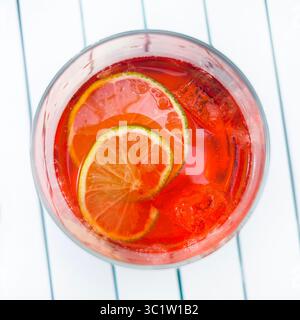 Cocktail alcolico Campari spritz in un bicchiere con fette di lime fresche e cubetti di ghiaccio sul tavolo. Direttamente sopra. Foto Stock
