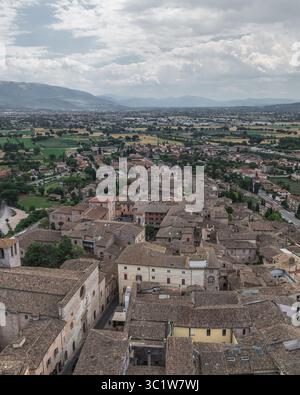 Veduta aerea dei tetti di terracotta baciati dal sole che scendono verso i lontani campi verdi e le montagne nebbiose, Spello, Umbria, Italia. Foto Stock