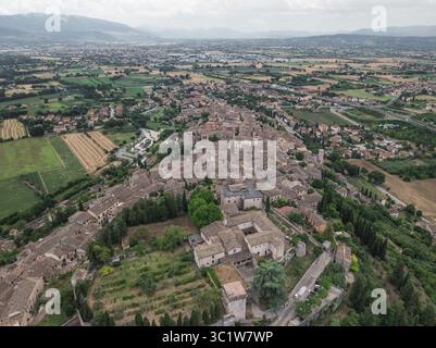 Vista aerea dei tetti in terracotta che scendono lungo le dolci pendici, incorniciati da campi verdeggianti e montagne lontane, Spello, Umbria, Italia. Foto Stock