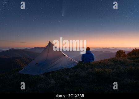 Viaggiatore vicino alla sua tenda sullo sfondo di un incredibile cielo stellato con cometa nelle montagne autunnali. I primi raggi del sole nel cielo stellato notturno. Fotografia di paesaggi Foto Stock