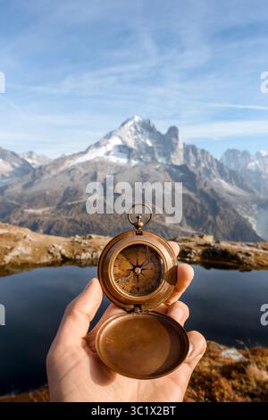 Il viaggiatore tiene la bussola in un'area alpina alta vicino al lago di montagna trasparente. Scena avventurosa con navigazione all'aperto, paesaggio panoramico e atmosfera da esplorazione escursionistica Foto Stock