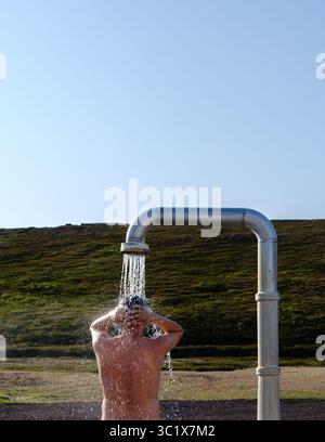 Un uomo gode di una rivitalizzante doccia termale calda in Islanda, circondato da splendidi paesaggi naturali. Le rilassanti cascate d'acqua scendono verso il basso, creando un'atmosfera serena. Un uomo alla Krafla Shower Foto Stock