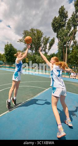 Due donne partecipano a una partita di basket su un campo all'aperto immerso nella luce del sole Foto Stock