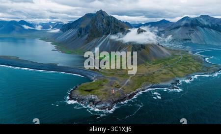 Splendida vista della costa frastagliata delle Icelands, caratterizzata da torreggianti montagne avvolte da nuvole, lussureggianti colline verdi e il suggestivo contrasto delle acque blu profonde. Riserva naturale delle Hvalnes Foto Stock