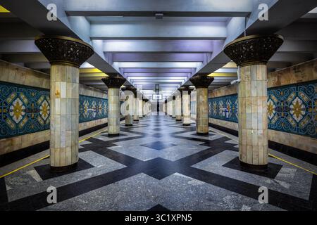 Tashkent, Uzbekistan - 5 aprile 2024: Vista della stazione della metropolitana di Alisher Navoi, dove le colonne ornate sorgono in mezzo a un pavimento a motivi geometrici, riflettendo il fresco e simmetrico bagliore delle luci della stazione. Foto Stock
