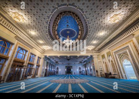 Tashkent, Uzbekistan - 5 aprile 2024: Vista dell'interno della moschea, con intricati motivi blu sul pavimento che contrastano con il soffitto ornato e il lampadario. Foto Stock