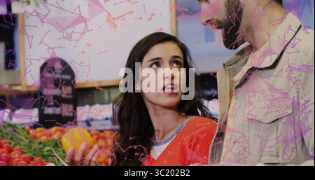 Tiene una donna al peperone giallo che chiacchiera con il partner nella stalla del mercato, con casse di pomodori Foto Stock