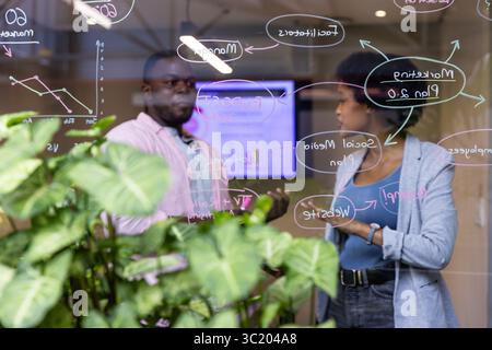 Colleghi afroamericani che collaborano al piano di marketing nella sala riunioni dell'ufficio con lavagna di vetro Foto Stock