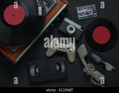 Intrattenimento e supporti retrò piatti. Lettore di dischi in vinile con registrazione in vinile, telecamera, videocassetta, audiocassetta, gamepad, ricevitore su un blac Foto Stock
