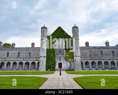 Galway, Irlanda - 13 giugno 2025: Maestoso edificio universitario a Galway, Irlanda, con edera che sale la facciata in pietra sotto un cielo dinamico. Foto Stock