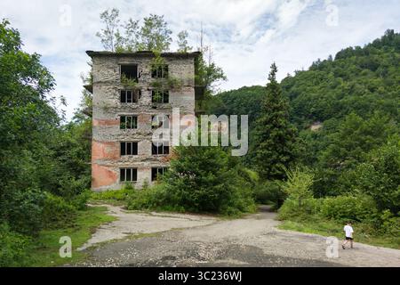 Paesaggio spettacolare della città di Akarmara, della città di Tkvarcheli, dell'Abkhazia. Vecchio edificio distrutto, rovine urbane ricoperte di piante verdi in estate Foto Stock
