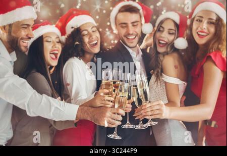 Amici diversi che brulicano con bicchieri di champagne la vigilia di Capodanno Foto Stock