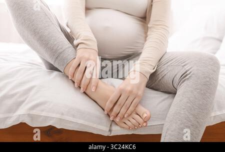 Donna incinta il suo massaggio piedi gonfi seduta sul letto Foto Stock