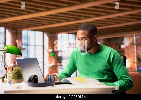 Uomo alla scrivania dell'ufficio domestico che utilizza un computer portatile, redige contratti, delineare termini, scrivere clausole, rivedere testi legali, salvataggio dei documenti, invio delle versioni finali a partner esterni Foto Stock