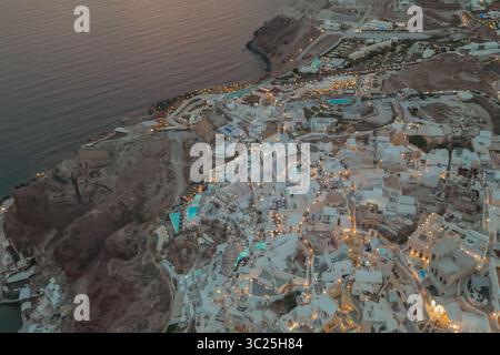 Oia, Santorini, Grecia. Vista serale dei droni con calde luci che illuminano le case bianche Foto Stock