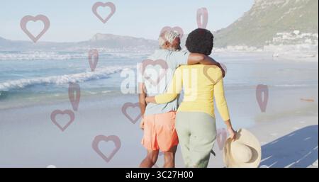 Walking Black Couple braccio in braccio lungo la spiaggia sabbiosa, con cappello di paglia a tegole larghe Foto Stock