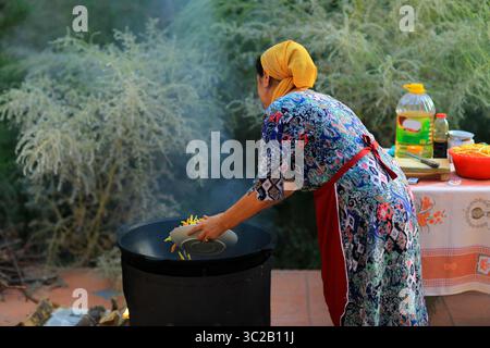 Preparazione di Samarkand plov. Le carote vengono aggiunte al calderone. Foto Stock