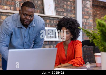 Colleghi afroamericani che collaborano con un computer portatile alla scrivania in ufficio con una tazza di caffè Foto Stock