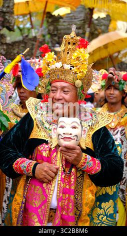 Uomo balinese in costume cerimoniale sorridente mentre tiene in mano una maschera tradizionale Foto Stock