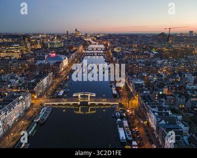 Vista aerea di ponti illuminati e barche che si riflettono nel canale sotto il cielo crepuscolo, Amsterdam, Olanda settentrionale, Paesi Bassi. Foto Stock