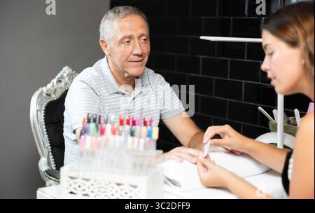 Uomo anziano che riceve manicure da una manicurista professionista in salone Foto Stock
