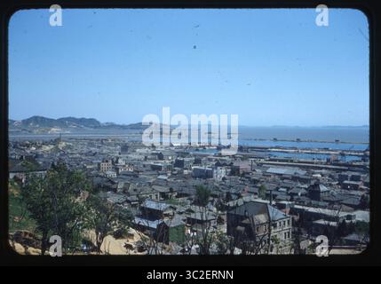Una vista panoramica di Incheon (precedentemente scritto Inchon), Corea del Sud, che guarda verso il Mar giallo, scattata il 6 giugno 1955. Un tempo importante centro industriale e porto marittimo, Incheon giocò un ruolo fondamentale nella guerra di Corea, in particolare durante lo sbarco anfibio del 1950 da parte delle forze ONU. Questa immagine cattura il recupero della città durante i primi anni del dopoguerra, mostrando edifici industriali, cantieri navali e isole circostanti. Dalla collezione di Wilfred K.C. Park, un militare della Marina degli Stati Uniti di stanza in Corea tra il 1955 e il 1957. Foto Stock