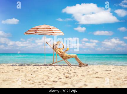 Donna seduta su una sedia a sdraio in riva al mare e sorseggiando un bicchiere di cocktail Foto Stock