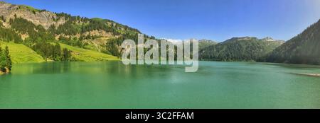 Ampia vista con un tranquillo lago delimitato da colline panoramiche e una natura vibrante che evoca tranquillità. Foto Stock