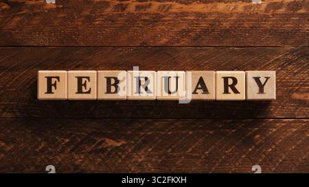 Parola February scritta in cubi di legno su sfondo marrone di legno Foto Stock