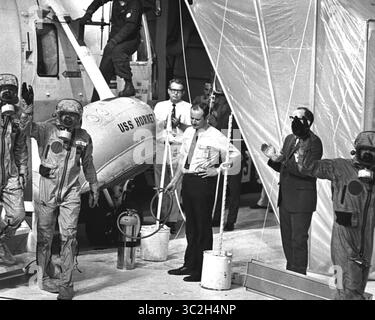 24 luglio 1969 - Florida, Stati Uniti - indossato in indumenti di isolamento biologico, i membri dell'equipaggio dell'Apollo 11, (L-R) Edwin Aldrin, Neil Armstrong (Waving), e Michael Collins escono dall'elicottero di recupero per salire a bordo della portaerei USS Hornet dopo lo schianto. L'operazione di recupero ha avuto luogo nell'Oceano Pacifico, dove i paracadutisti della Marina hanno recuperato la capsula che ospitava l'equipaggio di 3 uomini dell'Apollo 11. L'equipaggio fu trasportato in sicurezza a bordo della U.S.S. Hornet, dove furono piazzati in un Mobile Quarantine Facility (MQF). Questa struttura portatile è stata la loro casa fino a quando non hanno raggiunto la NASA ma Foto Stock