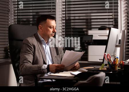 Il lavoratore d'ufficio stressava la digitazione su un notebook mentre la carta volava intorno a lui. Atmosfera aziendale travolgente, scadenze urgenti. Multitasking e cartaceo. Foto Stock