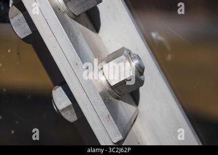 Primo piano del bullone e del dado in acciaio inox che fissano la piastra della trave angolata nella struttura industriale Foto Stock