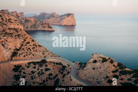 La vista aerea delle aspre scogliere di Cap de Formentor incontra il mare sereno e blu, mentre una strada tortuosa si snoda attraverso il paesaggio, Formentor, le Isole Baleari, Spagna. Foto Stock