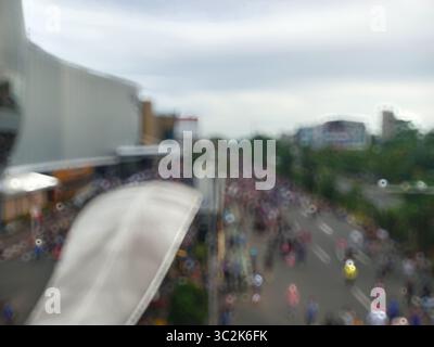 Vista sfocata di una folla di persone su una strada, con edifici su entrambi i lati sotto un cielo coperto, presi da una prospettiva alta Foto Stock
