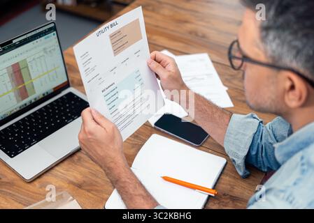 L'inquilino dai capelli grigi tiene a tavola una bolletta stampata con notebook e laptop in crescita Foto Stock