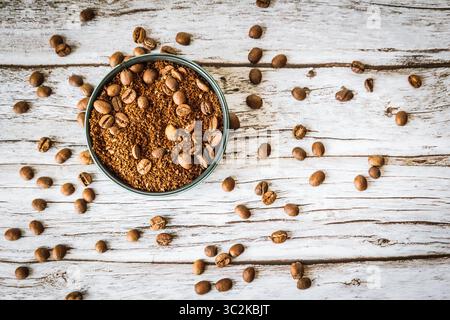 Vista dall'alto del caffè macinato cosparso di chicchi sparsi in una ciotola verde su un tavolo di legno intemprato, che evoca un aroma ricco, l'artigianato del barista e un accogliente slow-morn Foto Stock