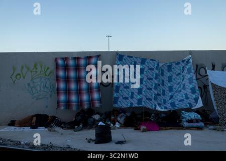 I migranti riposano sotto rifugi improvvisati accanto a muri ricoperti di graffiti, evidenziando le difficili condizioni affrontate al confine di Ciudad Juarez in mezzo alla crisi migratoria in corso. Foto Stock